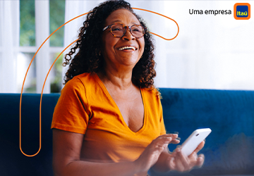 Uma senhora de pele negra, cabelos cacheados, utilizando óculos, sentada e sorrindo.